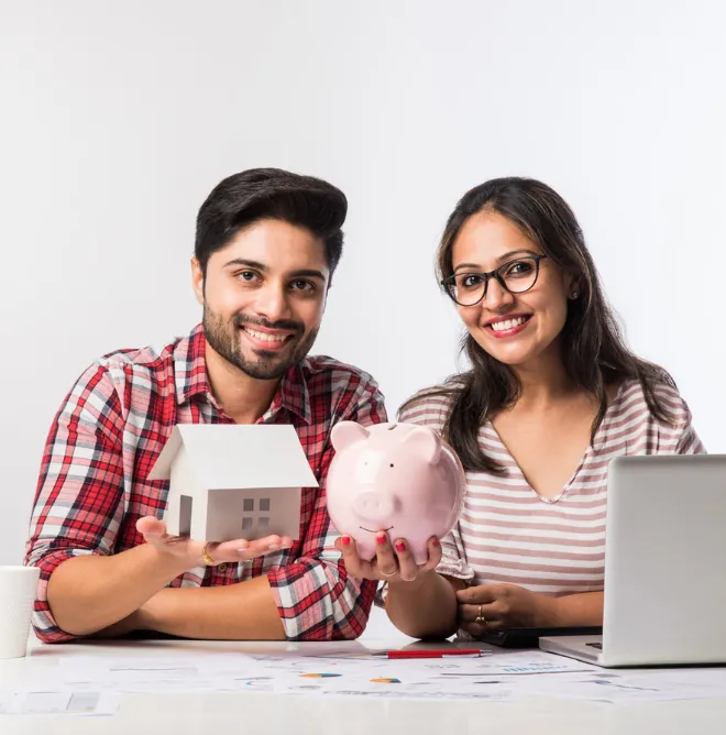 A young couple holding a model house and a piggy bank as they plan their home loan